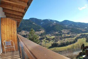 En balkon med gelænder i træ, der kigger ud over et bjerglandskab.