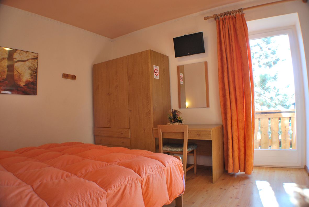 Un dormitorio con cama, armario de madera, escritorio y televisor.