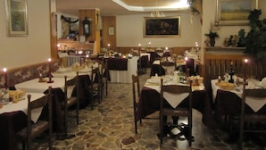 A restaurant with multiple tables set for dining, stone flooring, and a chandelier. - Albergo Lucia (Tesero)