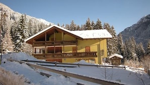 A two-story chalet with a balcony, surrounded by snow-covered trees and mountains. - Albergo Pozzole (Tesero)