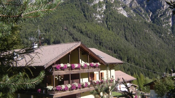 A chalet with a balcony adorned with flowers, set against a mountainous backdrop. - Albergo Pozzole (Tesero)