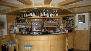 A bar area with wooden stools, a counter, and shelves stocked with bottles. - Albergo Pozzole (Tesero)