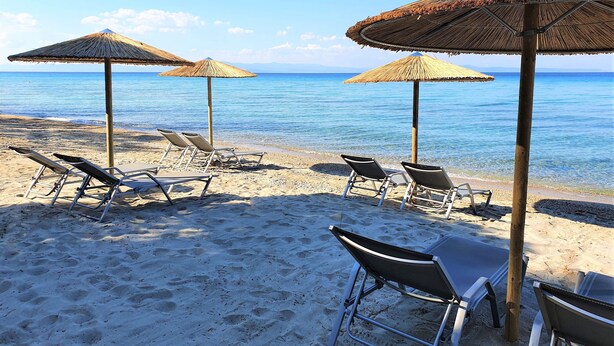Une plage avec des parasols en chaume et des chaises longues.