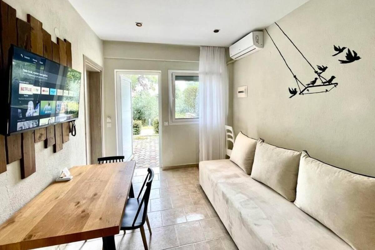 A living room with a wooden dining table, a beige sofa, a mounted TV, and a wall art of birds.