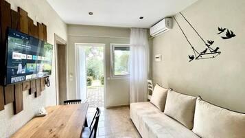 Un soggiorno con tavolo da pranzo in legno, un divano beige, una TV a parete e un quadro con uccelli.