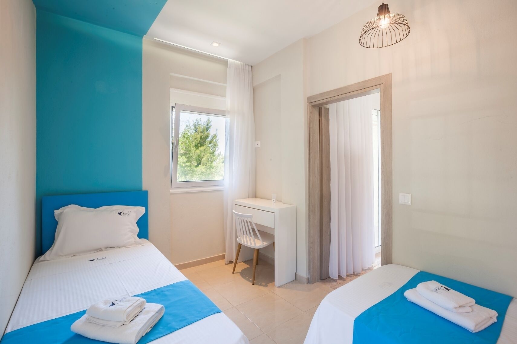 A hotel room with two beds, a desk, and a window.