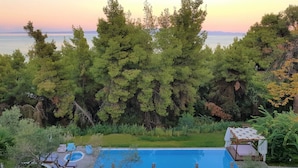 Un espace piscine doté de chaises longues et d’une terrasse en bois, entouré d’une végétation luxuriante et offrant une vue sur la mer.