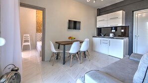 Une cuisine moderne avec des meubles blancs et un four encastré. On y trouve une table à manger avec quatre chaises et un téléviseur fixé au mur.