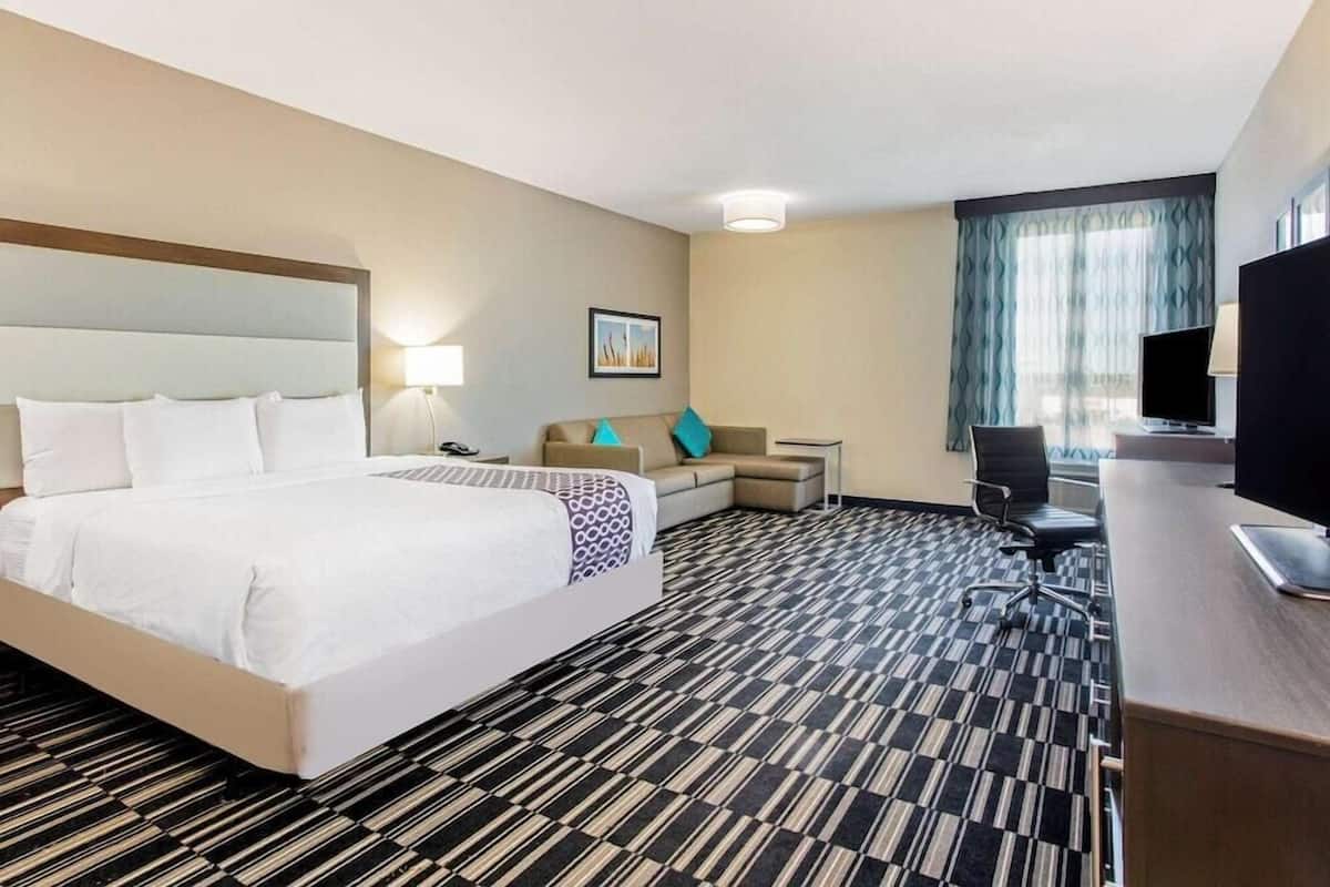 Ein Hotelzimmer mit einem großen Bett, einem Schreibtisch mit Computer, einem Sessel, einer Couch und einem Fernseher.