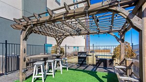 Eine Terrassengruppe im Freien mit einer Holz-Pergola, einem Grill und einer kleinen Sitzecke mit Hocker.