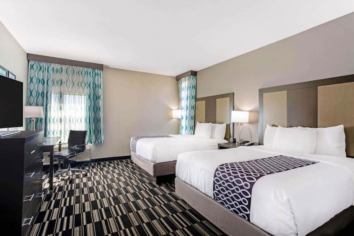 Ein Hotelzimmer mit zwei Betten, einem Schreibtisch, einem Stuhl und einem Fernseher.