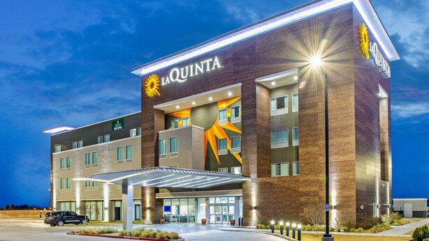 Ein La Quinta Hotel mit modernem Design, das ein auffälliges Sonnenmotiv an der Fassade, mehrere Stockwerke und einen überdachten Eingangsbereich zeigt.