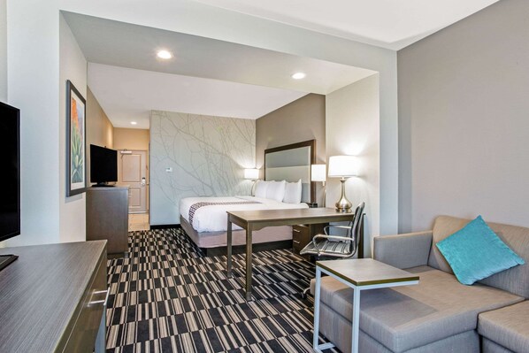 A hotel room with a bed, a desk, a chair, a television, and a sofa.
