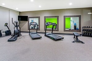 Une salle de sport équipée de tapis de course, d’un appareil elliptique, d’un banc de musculation et d’un porte-haltères.