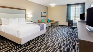 Ein Hotelzimmer mit einem großen Bett, einem Schreibtisch, einem Sessel, einem Fernseher und einem Fenster mit Vorhängen.