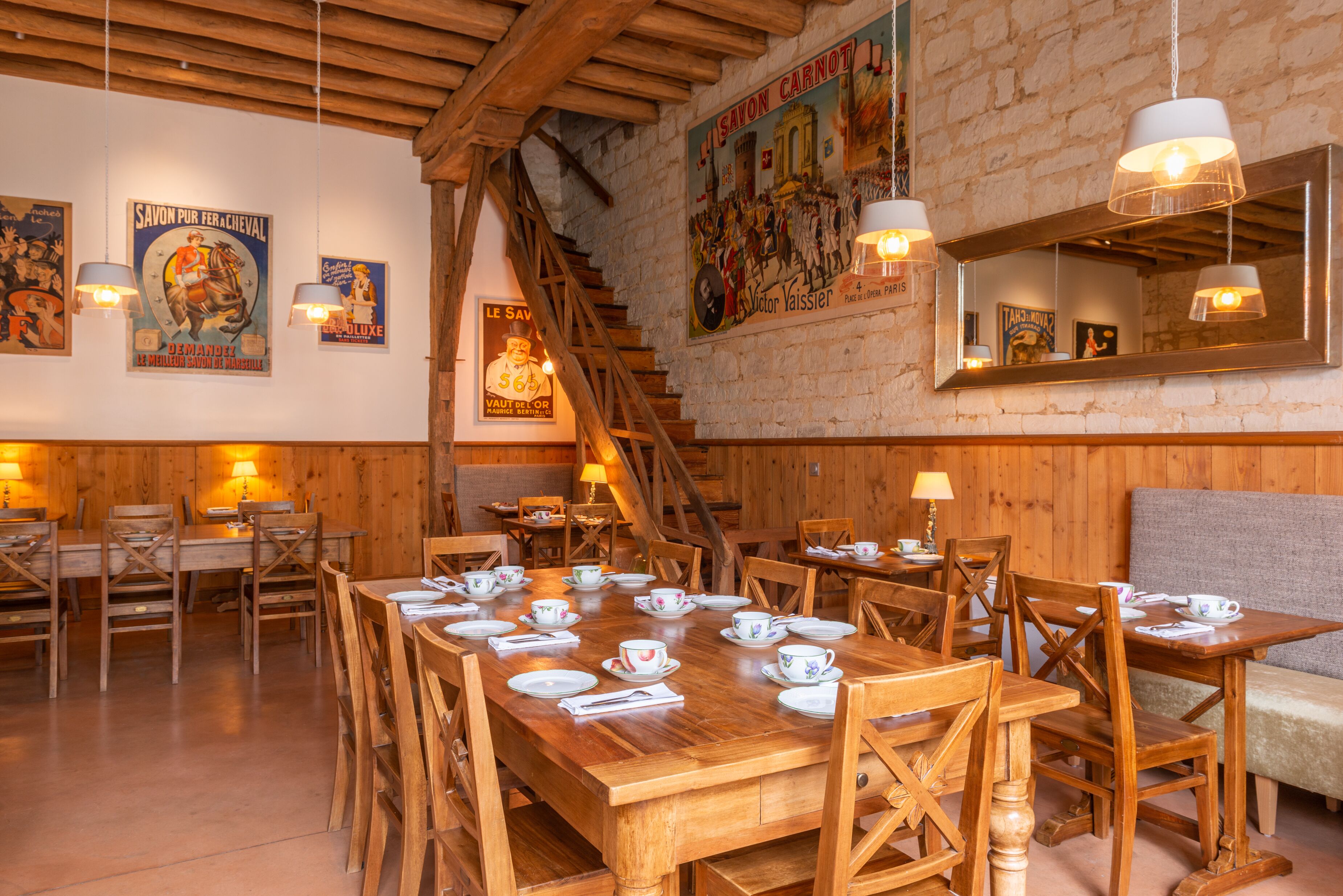 A restaurant with wooden tables and chairs, a staircase, and various posters on the walls.