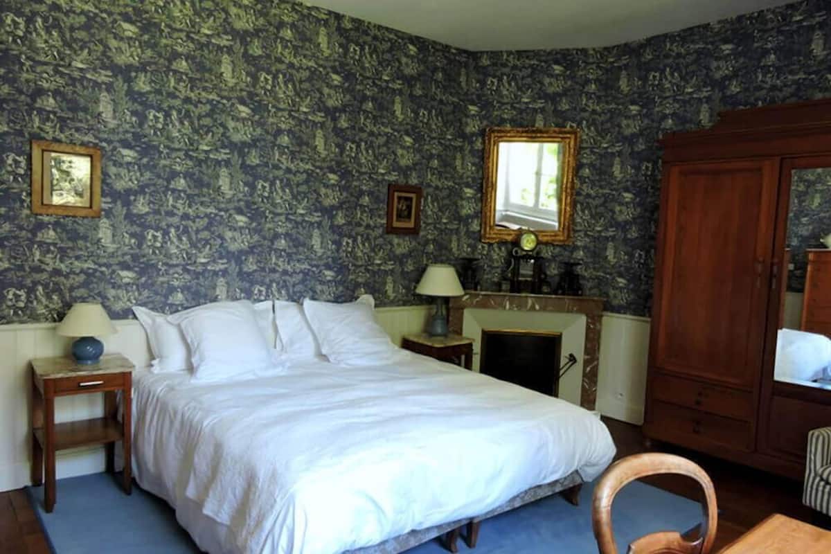 Une chambre à coucher avec un grand lit, une table de chevet, une lampe, une cheminée et une armoire.