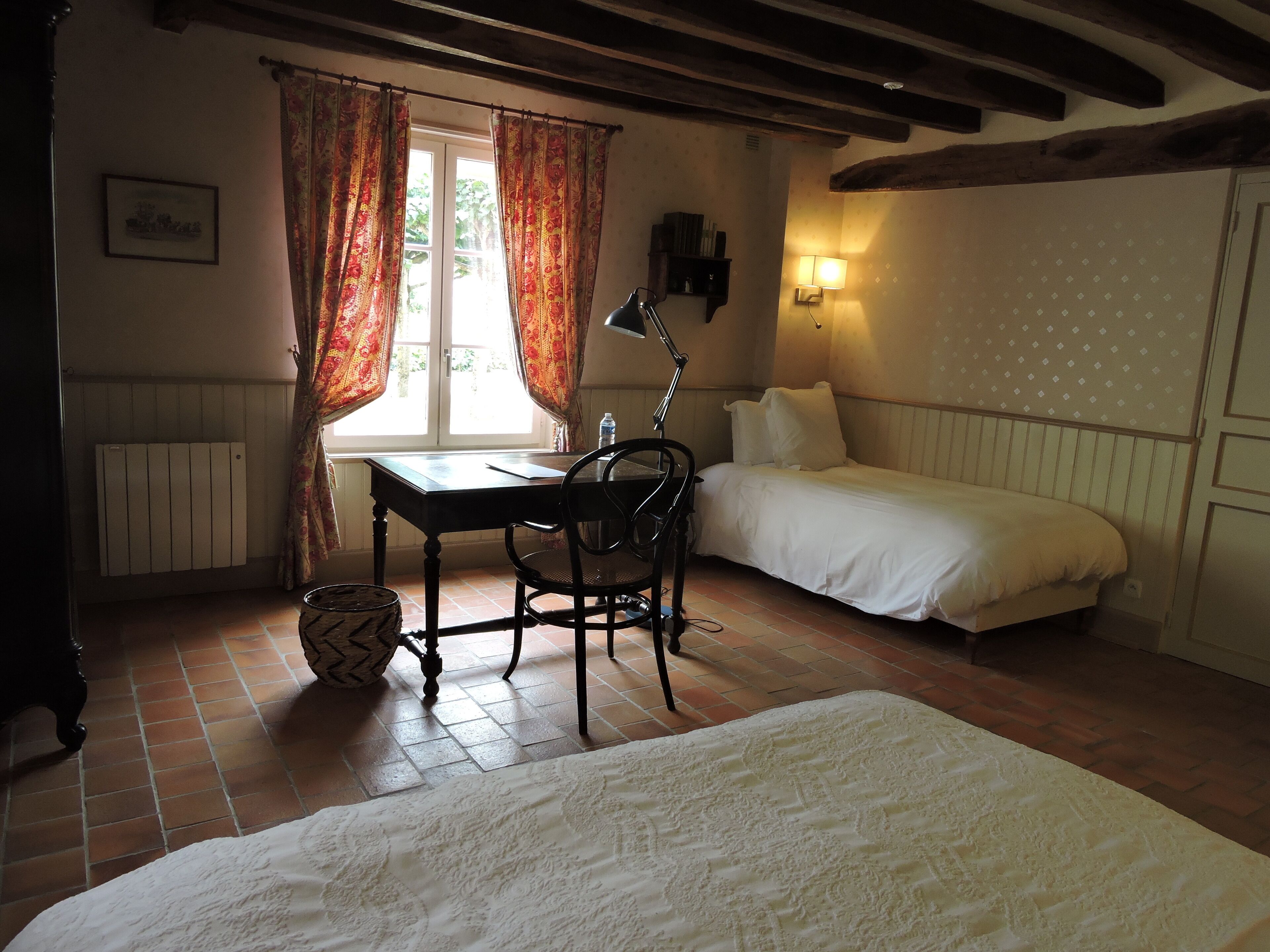 Une chambre avec un lit simple, un bureau avec une chaise, un radiateur et une fenêtre avec des rideaux.