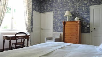 Ein Schlafzimmer mit einem Bett, einem Holzkleiderschrank, einem Stuhl, einem Schreibtisch und einem Fenster mit Vorhängen.