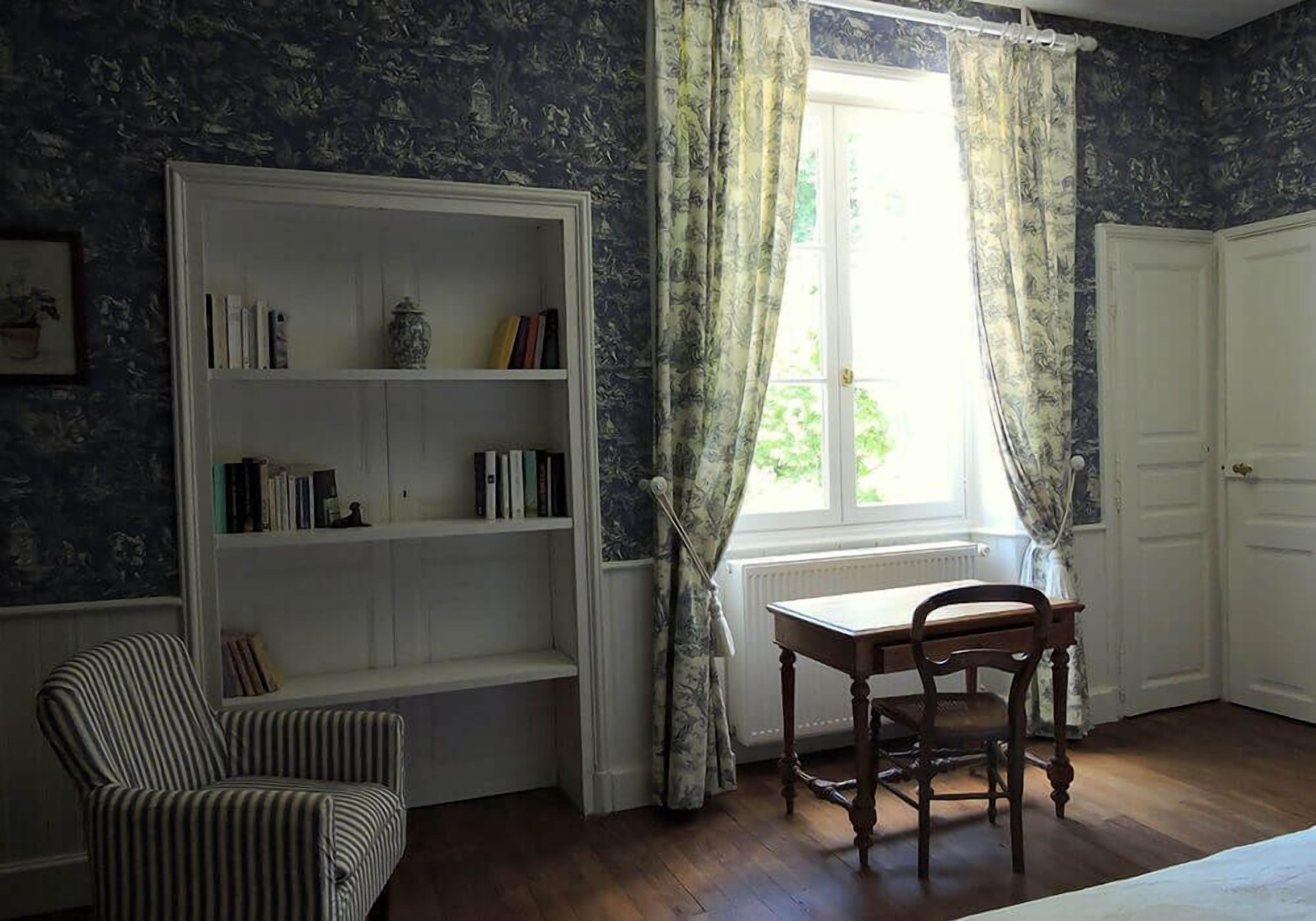 A room with a bookshelf, a chair, a table, and a window with curtains.