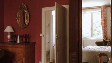 Una habitación con un aparador de madera, un espejo, una cama con colcha estampada y una ventana con cortinas.