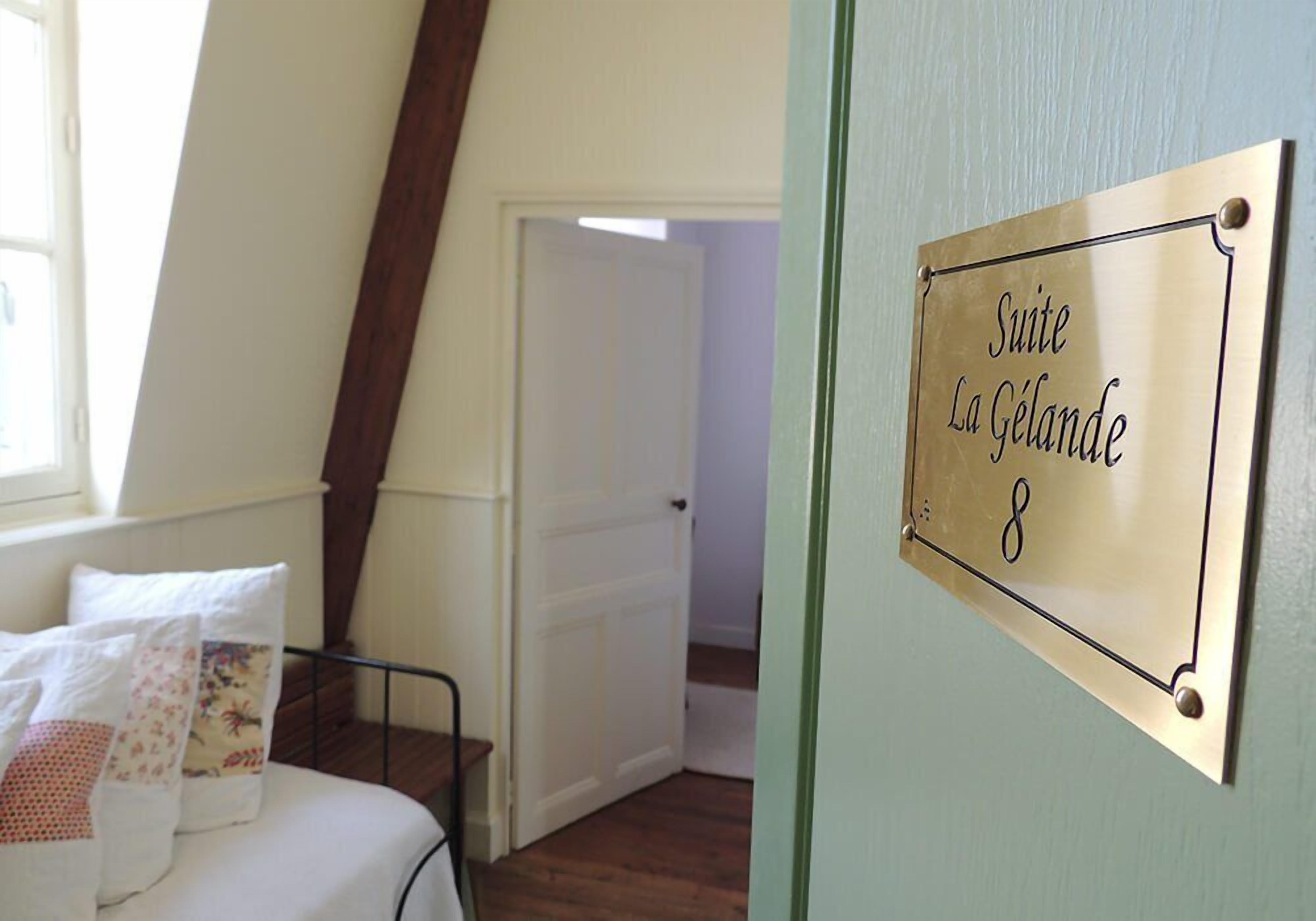 A room with a bed, a brass sign reading "Suite La Gélande 8", and a door leading to another room.