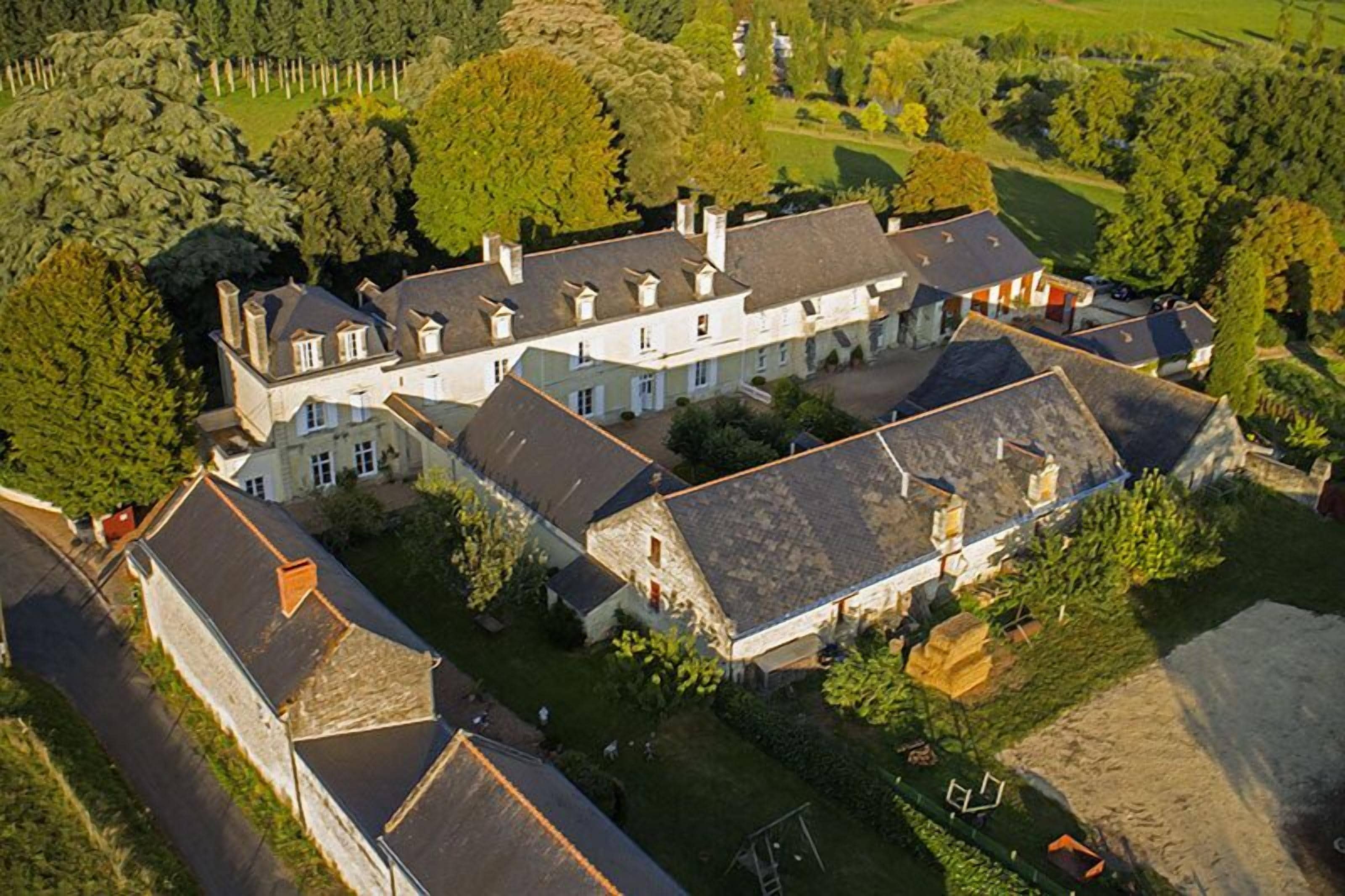 An aerial view of a large estate with multiple buildings, including a main house and several outbuildings, surrounded by lush greenery and a well-maintained lawn.