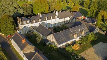 An aerial view of a large estate with multiple buildings, including a main house and several outbuildings, surrounded by lush greenery and a well-maintained lawn.