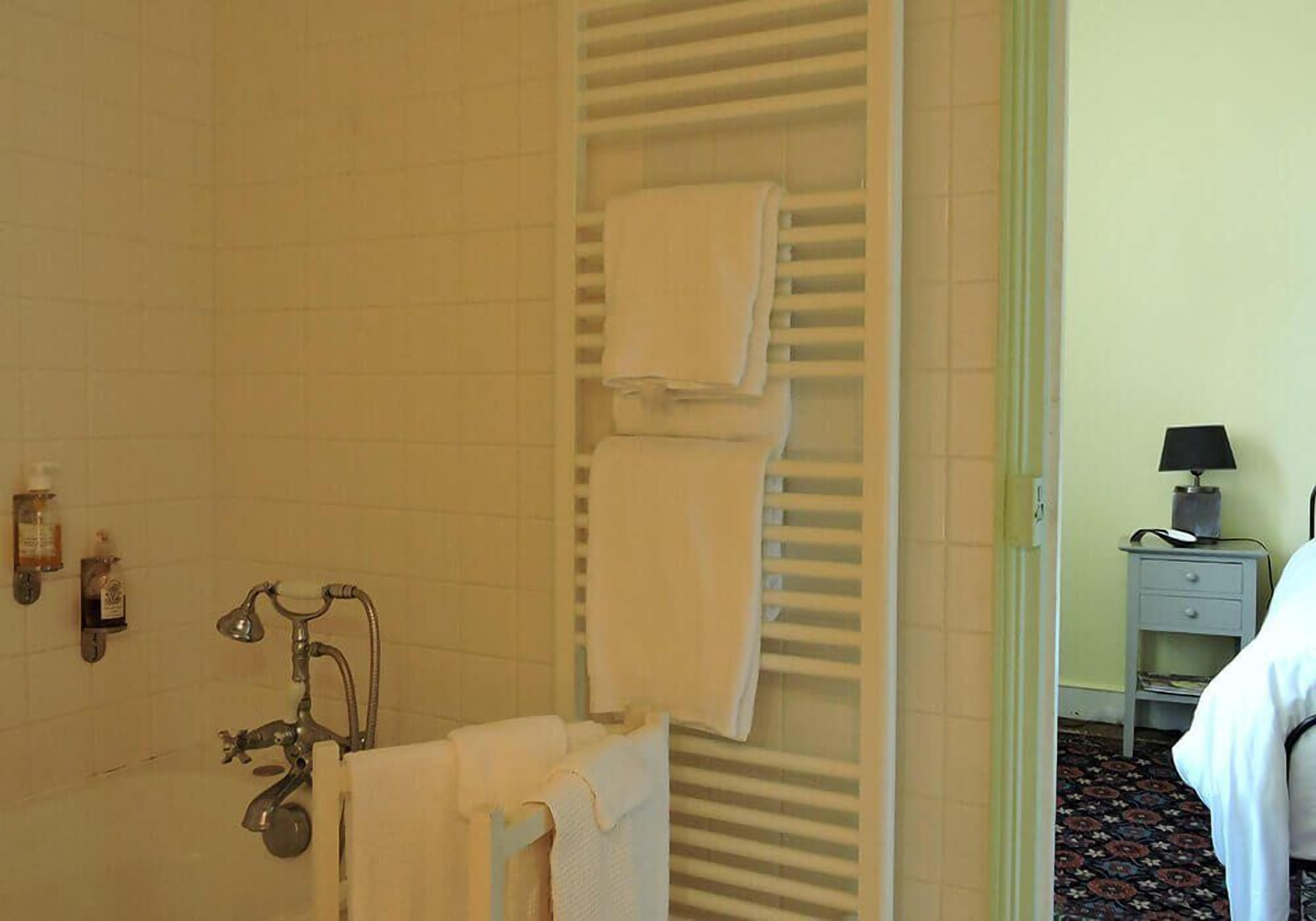 A bathroom with a bathtub, a towel rack with folded towels, a small shelf with toiletries, and a nightstand with a lamp.