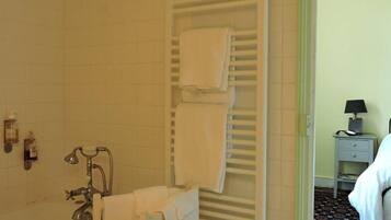 A bathroom with a bathtub, a towel rack with folded towels, a small shelf with toiletries, and a nightstand with a lamp.