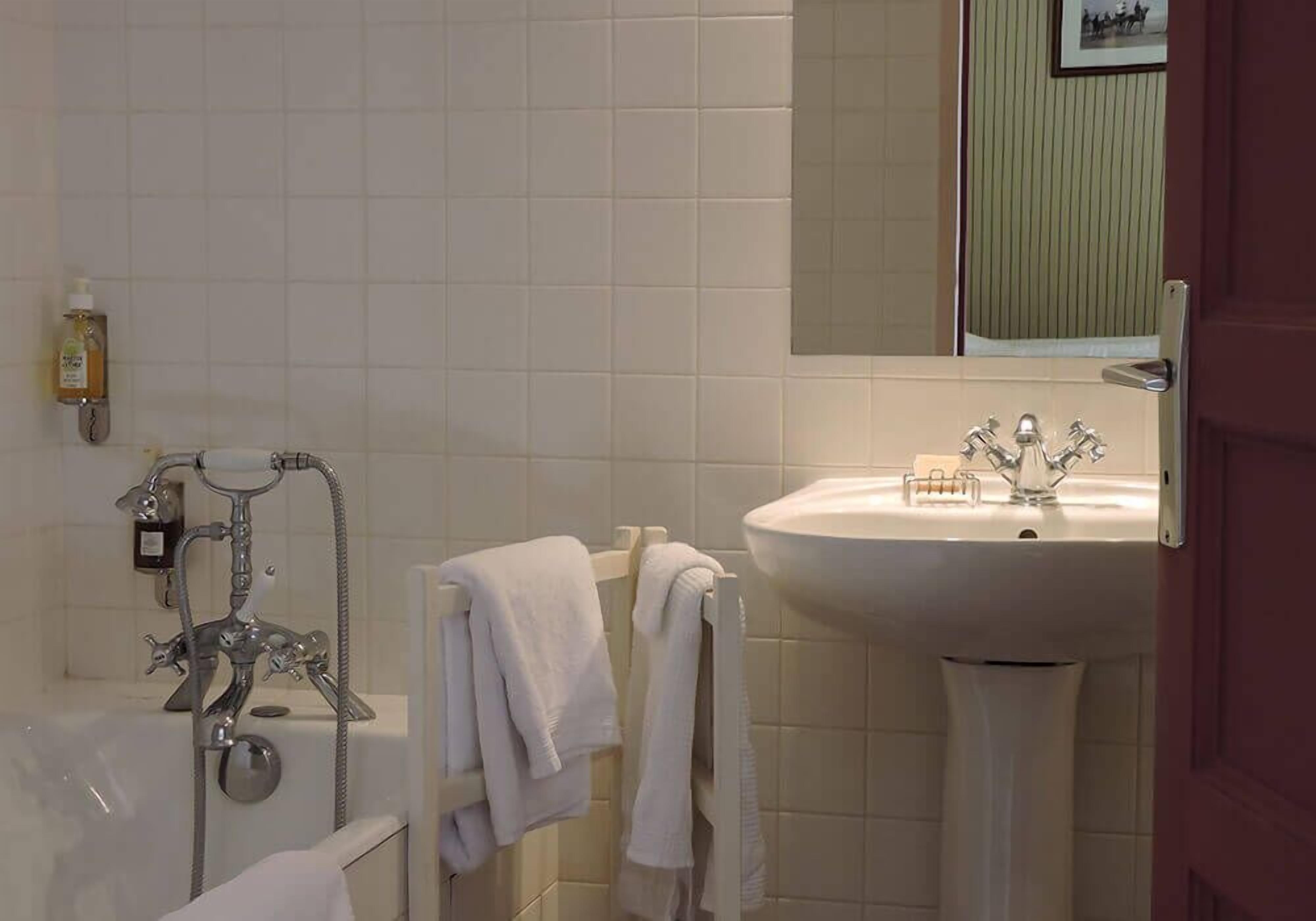 A bathroom with a bathtub, a sink, and a mirror. There are towels hanging on a rack.