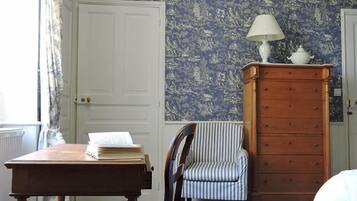 Una habitación con un escritorio de madera, una silla a rayas, un aparador con una lámpara y un papel tapiz estampado.