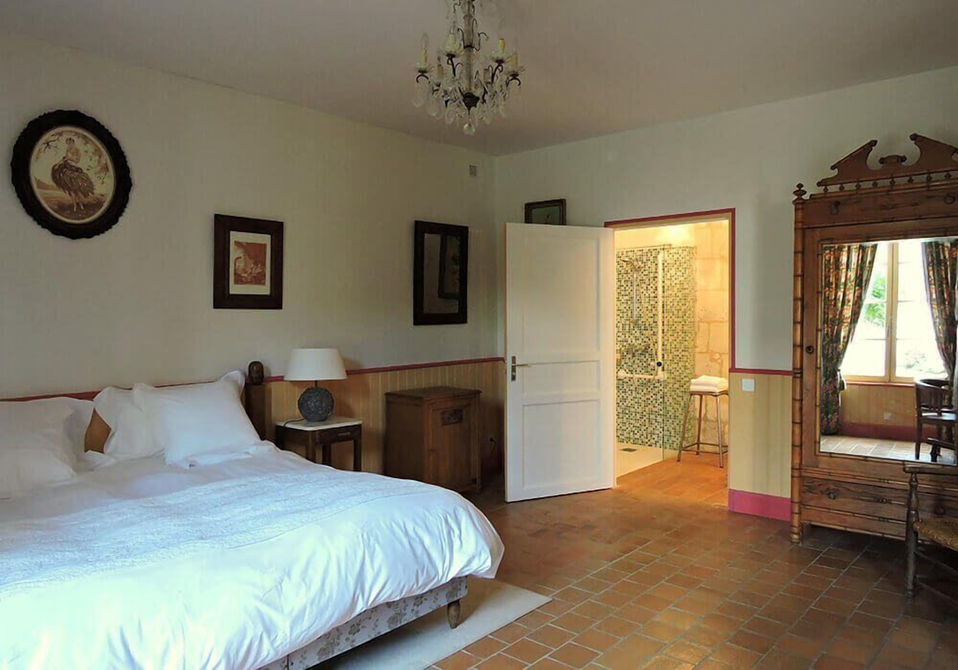A bedroom with a bed, a nightstand, a dresser, a mirror, and a door leading to another room.