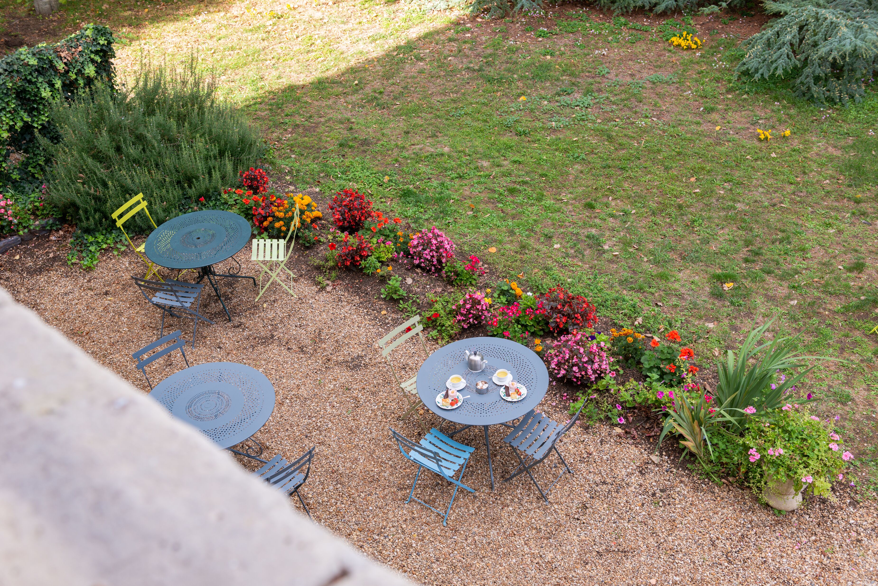 Un patio al aire libre con dos mesas redondas y cuatro sillas, rodeado de una variedad de flores y plantas coloridas.