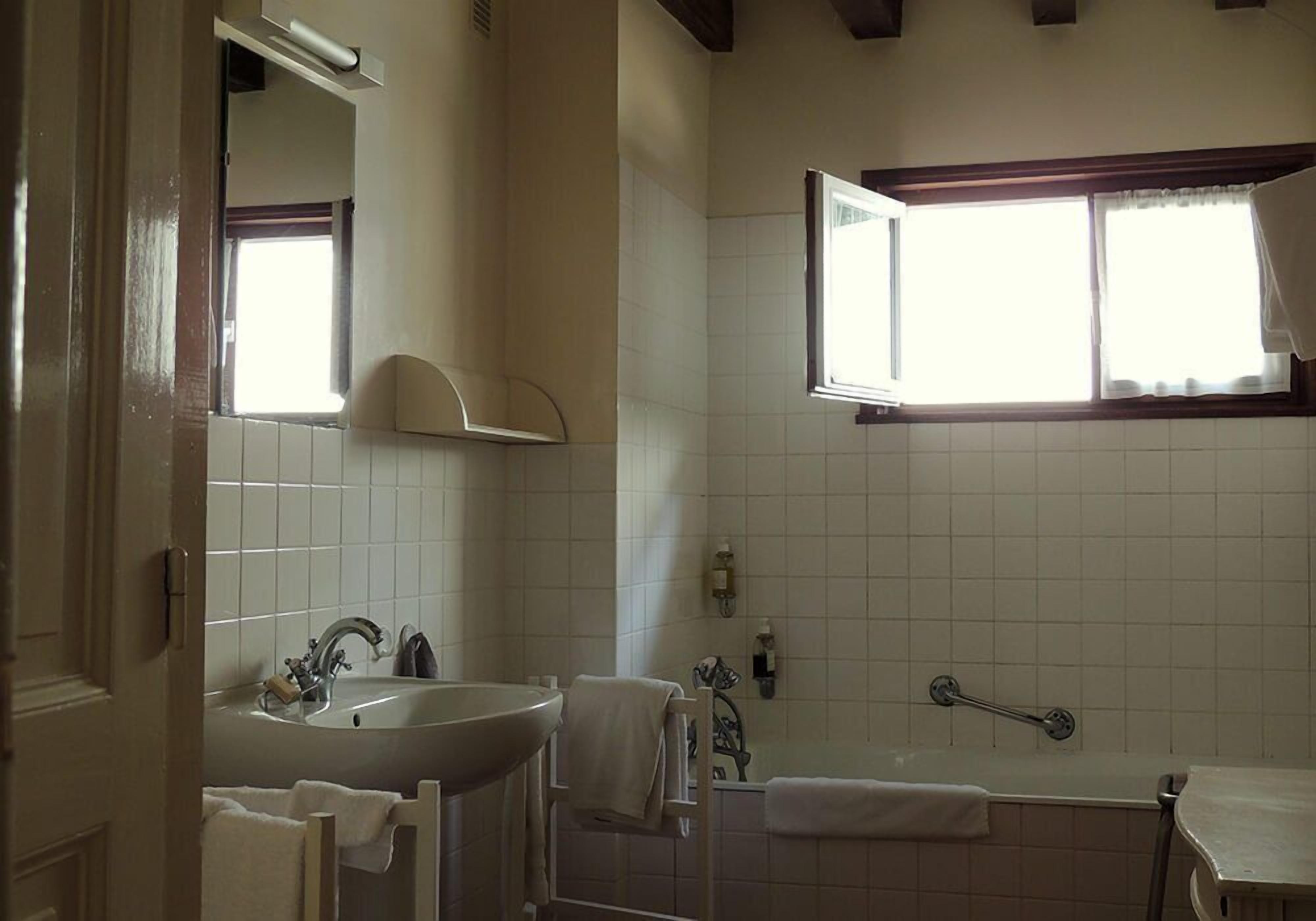 A bathroom with a sink, mirror, window, and bathtub.