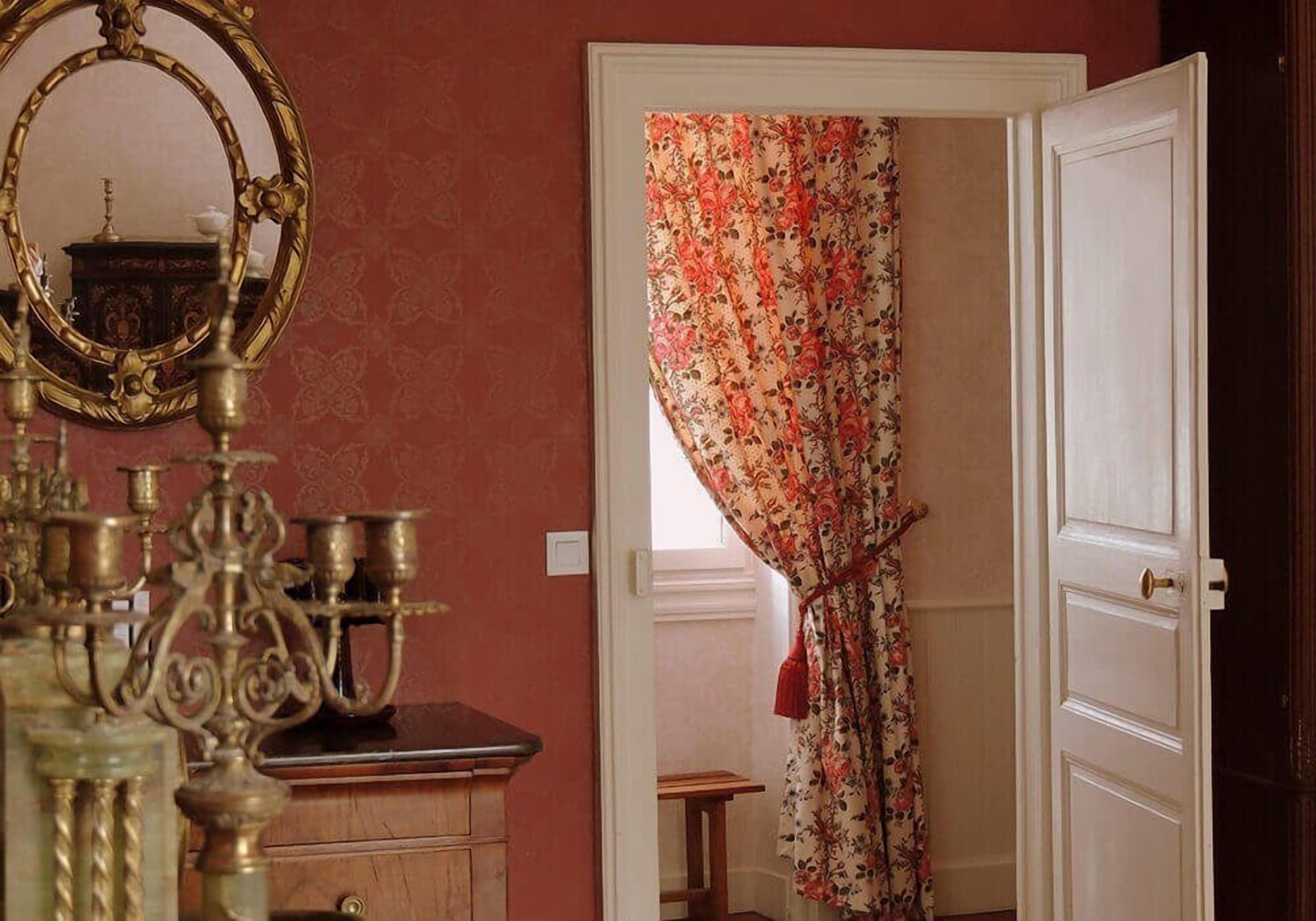 Una habitación con espejo, cómoda y puerta con cortinas florales.