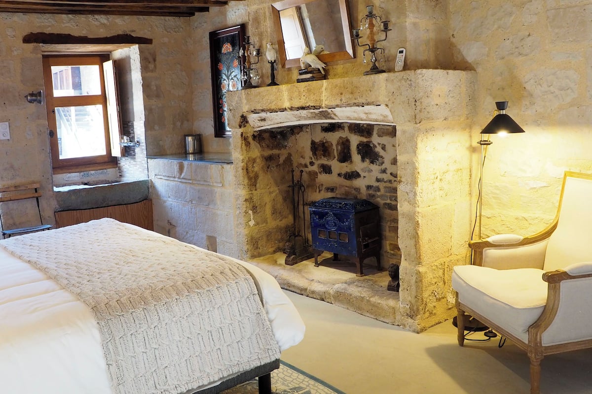 Une pièce chaleureuse avec une cheminée en pierre, un lit, une chaise et un plafond en bois.
