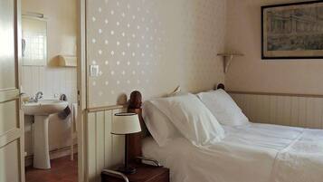 Un dormitorio con cama, mesita de noche con lámpara, cuadro en la pared y baño con lavabo y espejo.