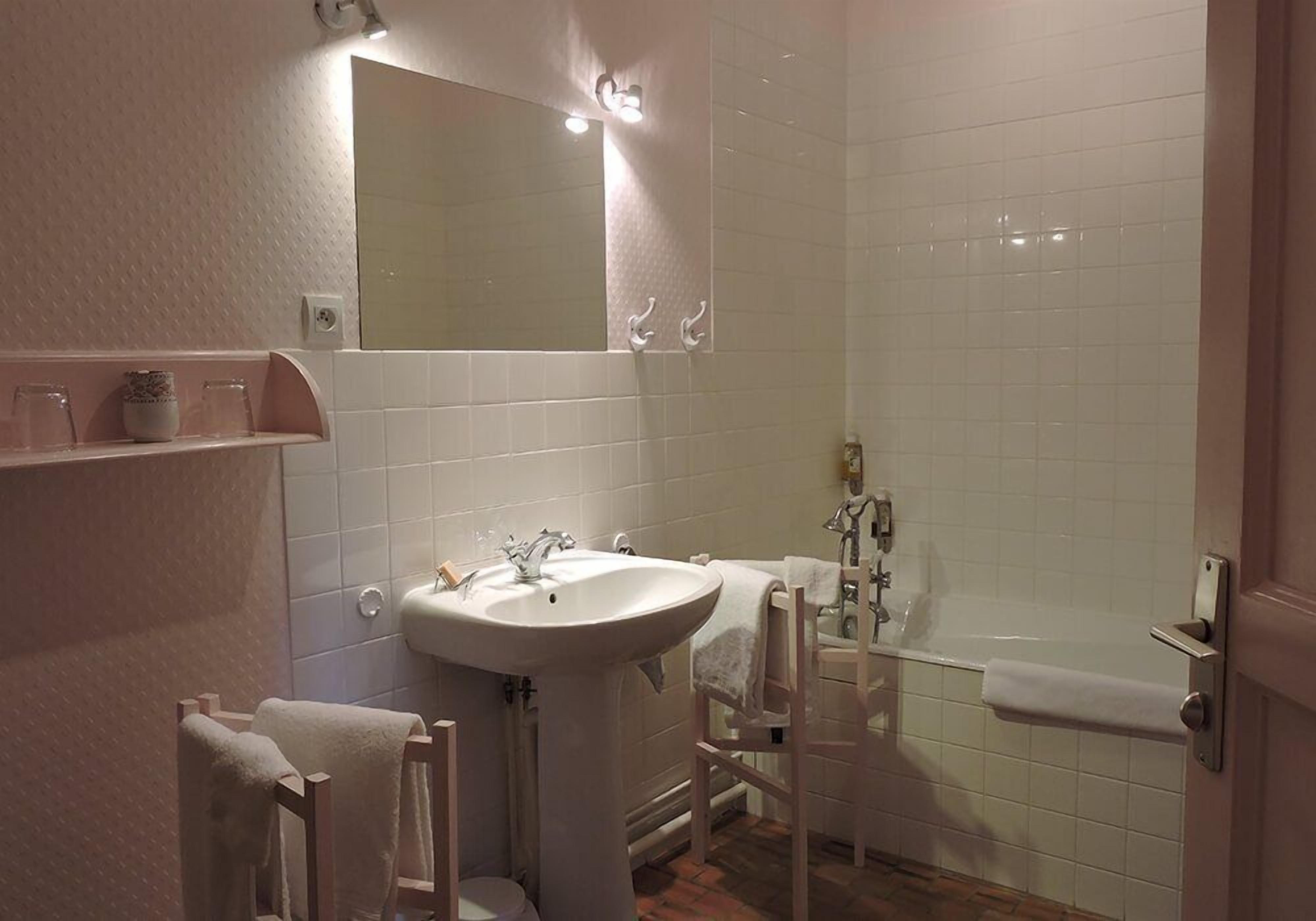 A bathroom with a sink, mirror, and bathtub. There are towels hanging on a rack and a shelf with jars.
