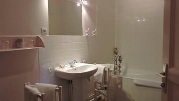 A bathroom with a sink, mirror, and bathtub. There are towels hanging on a rack and a shelf with jars.