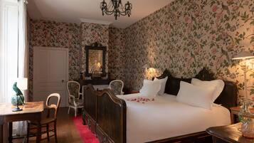 A bedroom with a large bed, a chandelier, floral wallpaper, and a wooden dresser.
