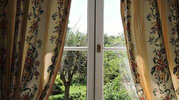 A door with floral curtains, a view of greenery outside, and a tree in the background.