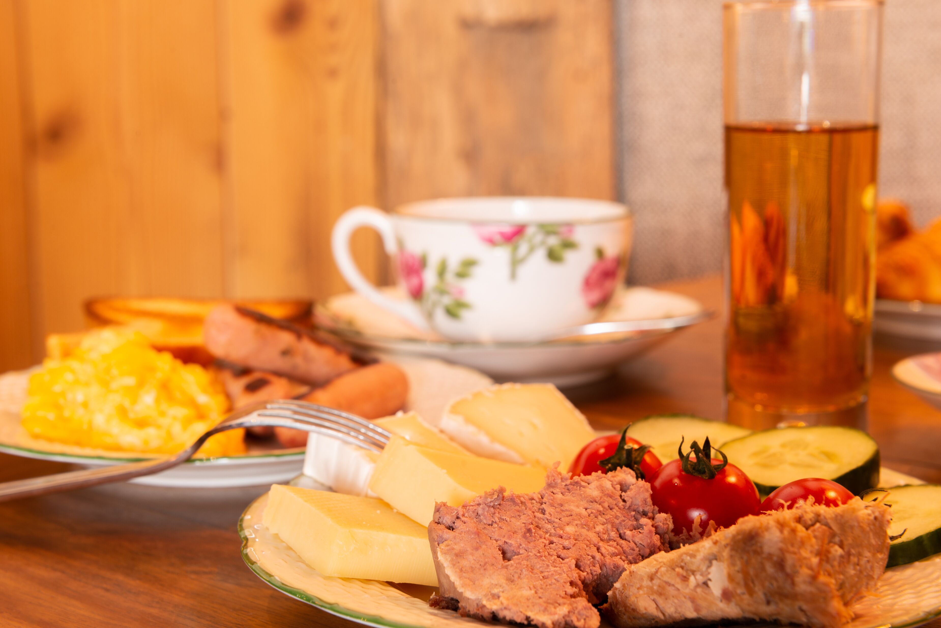 Une table dressée avec des assiettes remplies de nourriture, notamment du fromage, de la viande et des légumes, une tasse de thé et un verre d’eau.