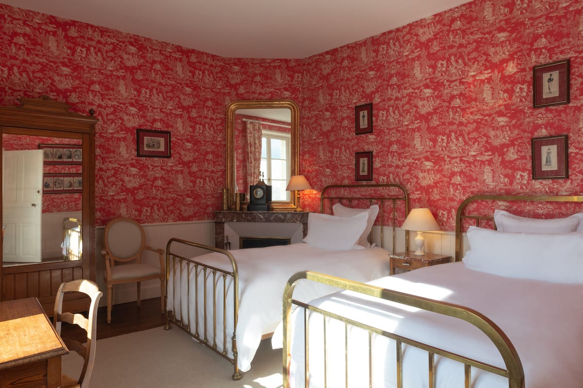 Une chambre avec deux lits, une chaise en bois, un miroir et une commode.