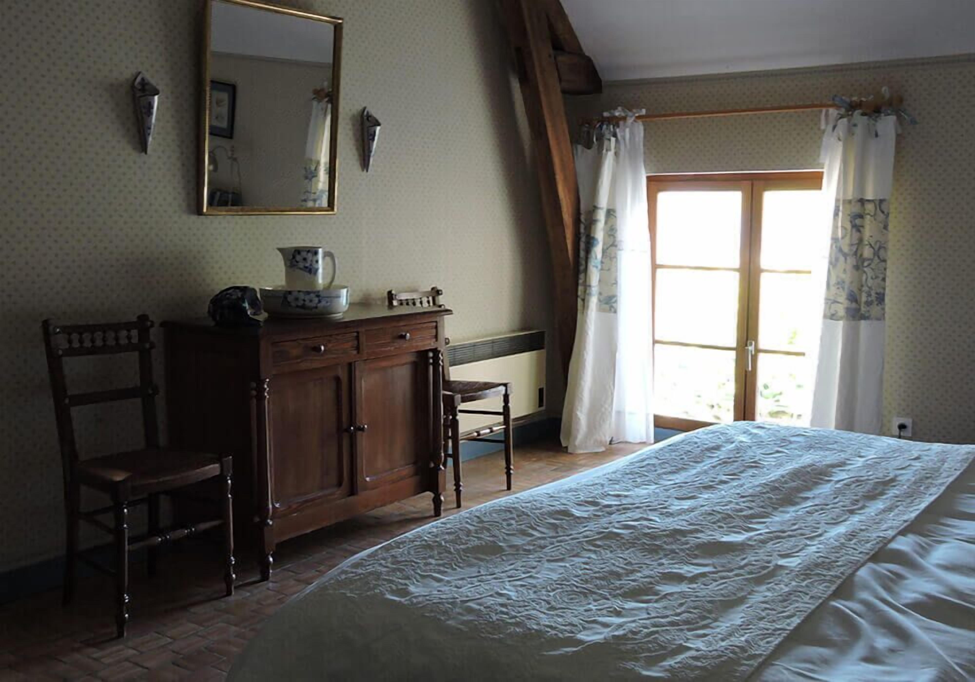 Un dormitorio con cama, cómoda de madera, una silla y una ventana con cortinas.