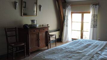 Un dormitorio con cama, cómoda de madera, una silla y una ventana con cortinas.