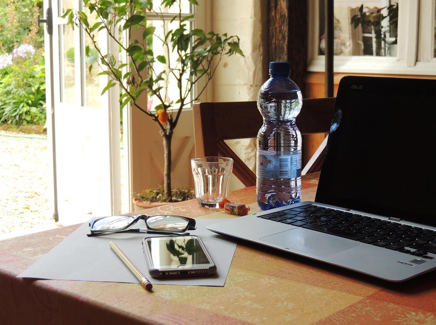 Un ordinateur portable est posé sur une table, à côté d’une bouteille d’eau, d’un téléphone intelligent, d’une paire de lunettes et d’une petite plante.
