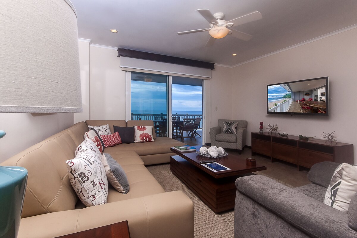 A modern living room with a large sofa, a coffee table, and a television mounted on the wall.