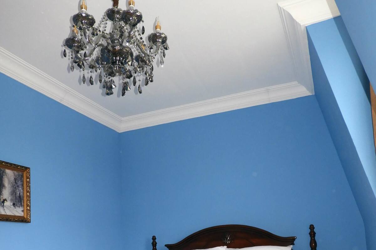 A bedroom with a wooden bed, two bedside tables with lamps, a chandelier, and a framed picture on the wall.