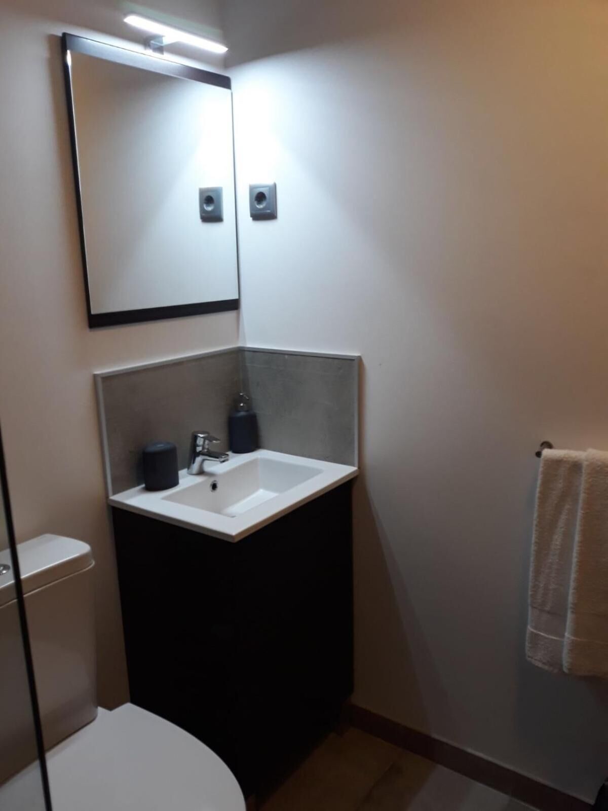 Un baño pequeño con un lavamanos blanco, un espejo y una toalla colgada en la pared.